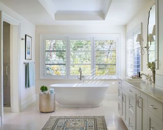 bathroom with cream walls, white freestanding bath, large windows and neutral color scheme