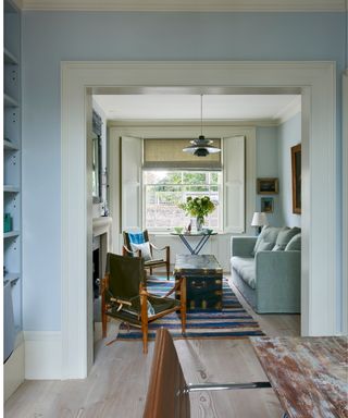 blue painted living room with a connecting dining room painted in the same blue with blue sofa and a rustic dining table