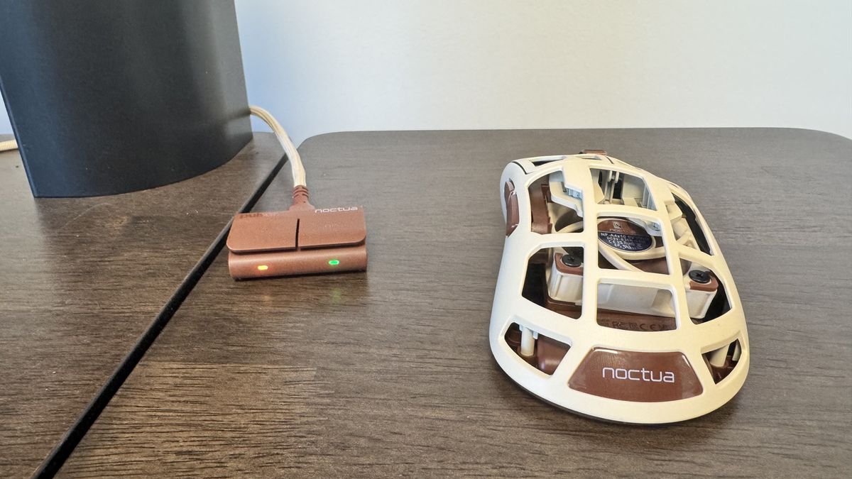 The Pulsar Feinmann F01 Noctua Edition gaming mouse to the right of its dongle on a wooden desk