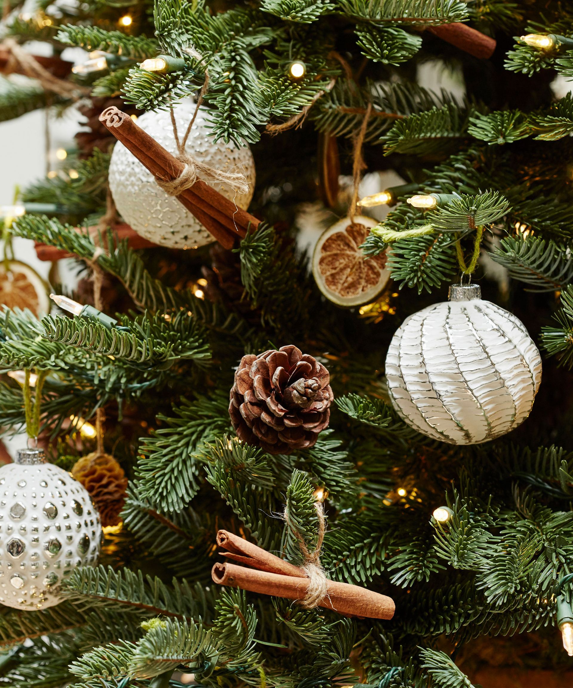 Μια κινηματογράφηση σε πρώτο πλάνο με λευκά glitter χριστουγεννιάτικα στολίδια, κουκουνάρια και φέτες αποξηραμένων φρούτων και ξυλάκια κανέλας σε ένα χριστουγεννιάτικο δέντρο.