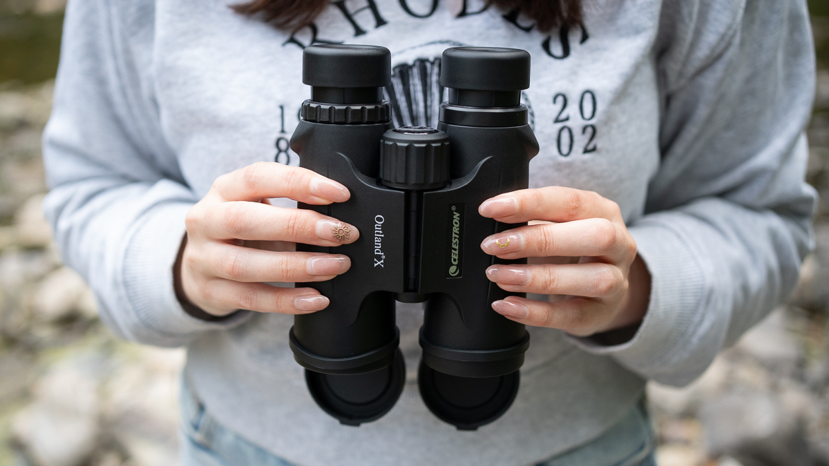 woman using the Celestron Outland X 10x42 binoculars next to a river