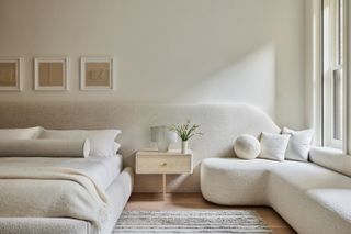 white bedroom with extended headboard that continues into window seat, all white bedding, and floating timber nightstand