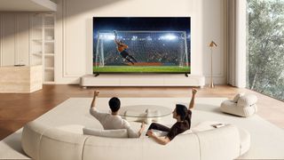Lifestyle image showing two people watching soccer on the TCL X11L SQD Mini-LED TV in a living room environment.