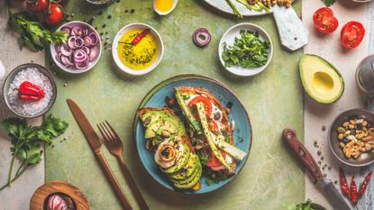 Best meal prep delivery services. Sweet potatoes sandwich avocado, egg, tomatoes and asparagus served on green kitchen table with ingredients: fresh vegetables, seasonings, olives oil and cutlery. Top view. Healthy lunch.