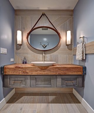 Wooden bathroom vanity with round hanging mirror and wall sconces