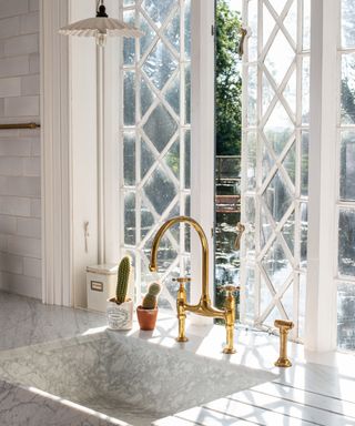 devol kitchen with a huge sunlit window, marble sink and brass faucets