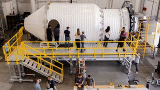 A series of people stand around a large space station in a giant warehouse