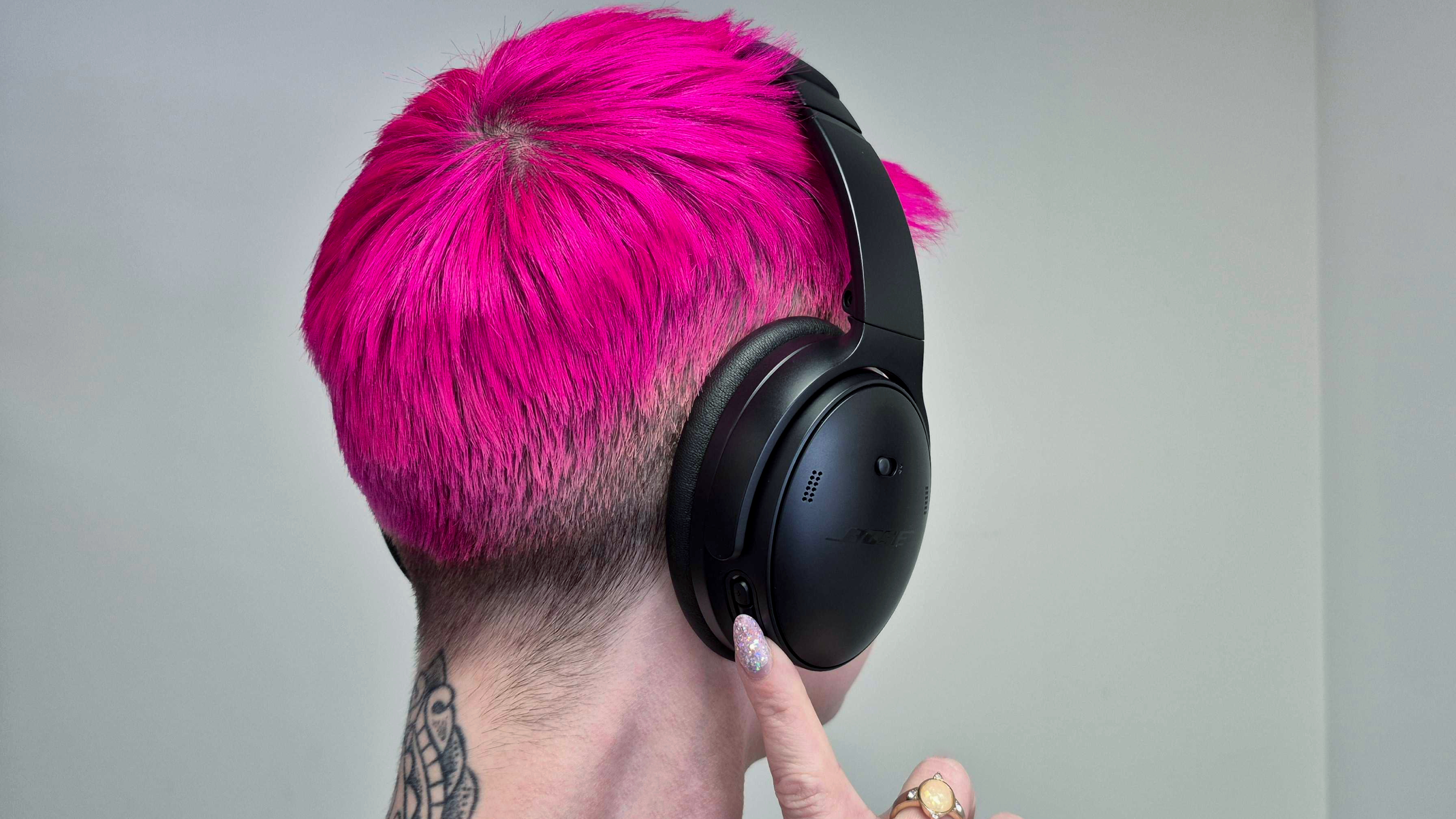 A woman is pressing a button on the black Bose QuietComfort headphones she's wearing.