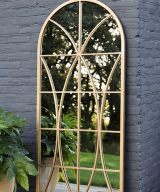gold frame garden mirror leaning against a grey painted wall