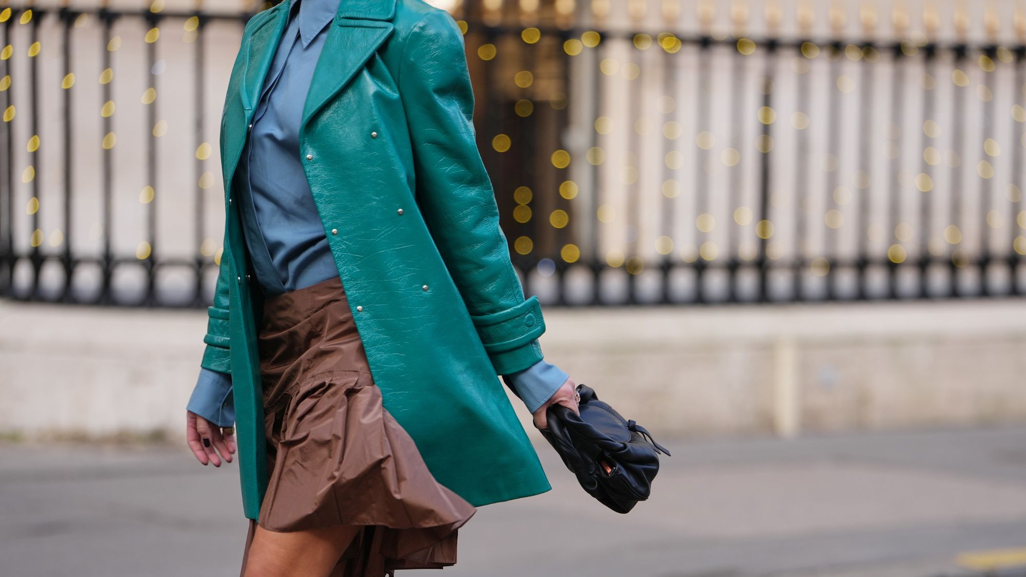 street style shot of woman wearing turquoise trench, blue shirt, brown nylon skirt and white sheer knee high socks