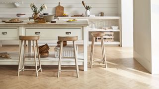 Pale wood-look vinyl flooring in a white and cream kitchen with wooden stools.