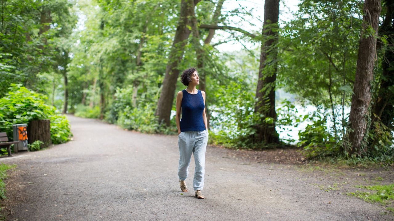 Woman walking on road in forest. Full length of female is exploring while hiking in woods. She is wearing casuals.