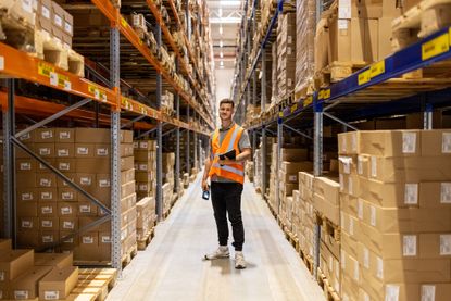 A young, male worker takes inventory in a warehouse full of boxes