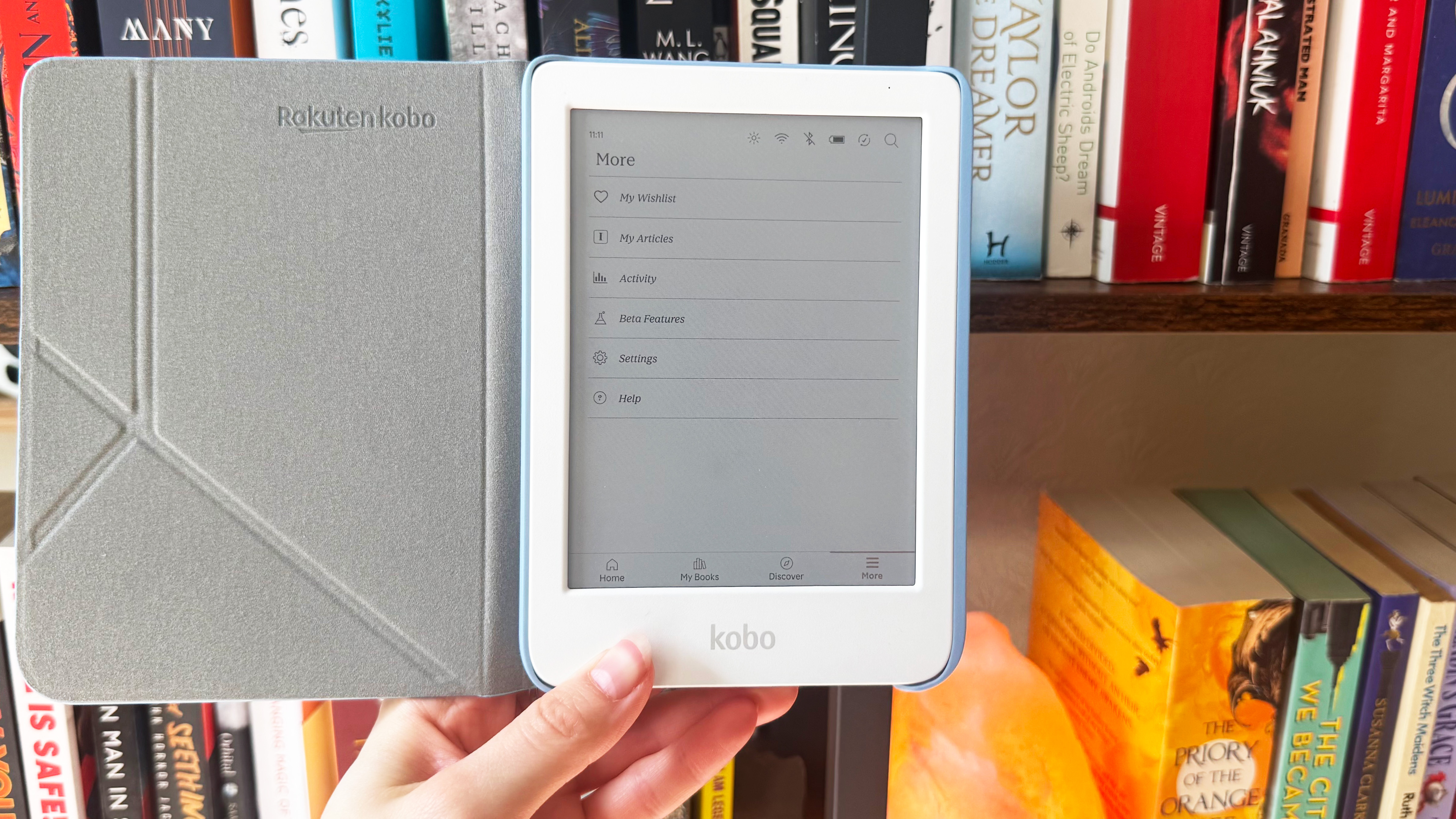 a photo of the kobo clara colour against a bookshelf, showing the sleep cover and settings page