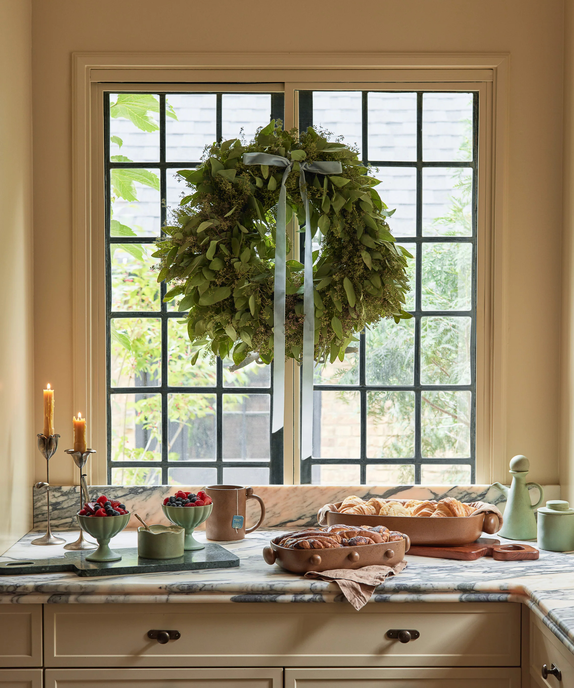 a kitchen with food on the countertop and a decorative wreath hanging from the window with a blue ribbon bow