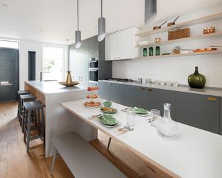 a modern kitchen with island and dining table, grey and white cabinets and statement lighting Pluck JamesLane