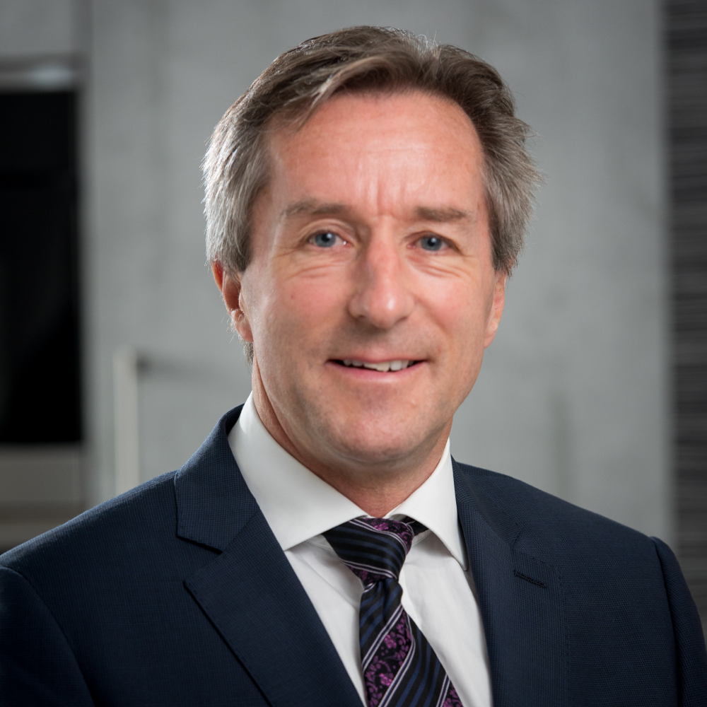 male with short grey hair wearing navy suit, white shirt and tie