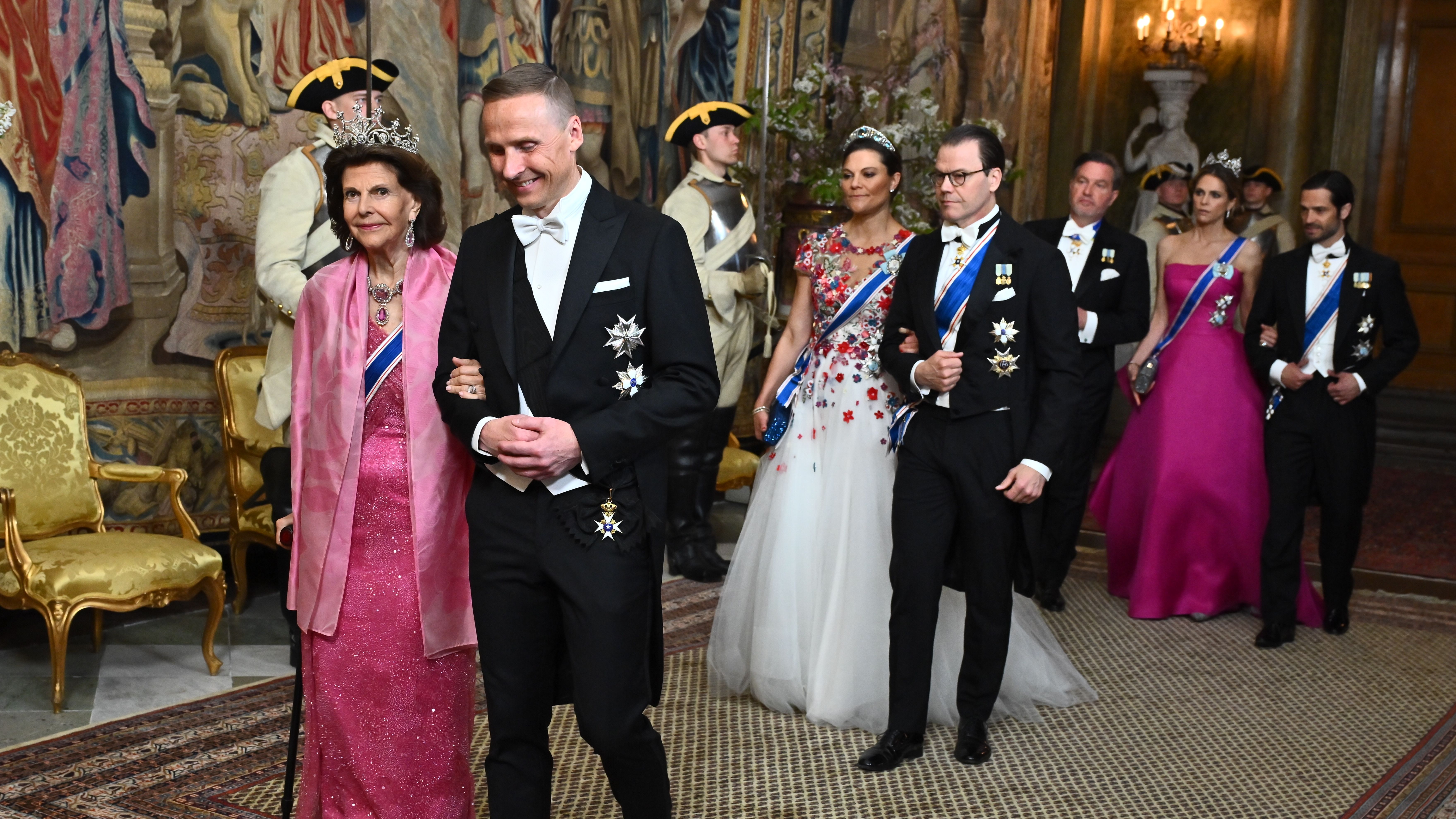 Queen Silvia, Crown Princess Victoria, Prince Daniel, Princess Madeleine and Prince Carl Philip wearing tuxes and tiaras walking into a state banquet