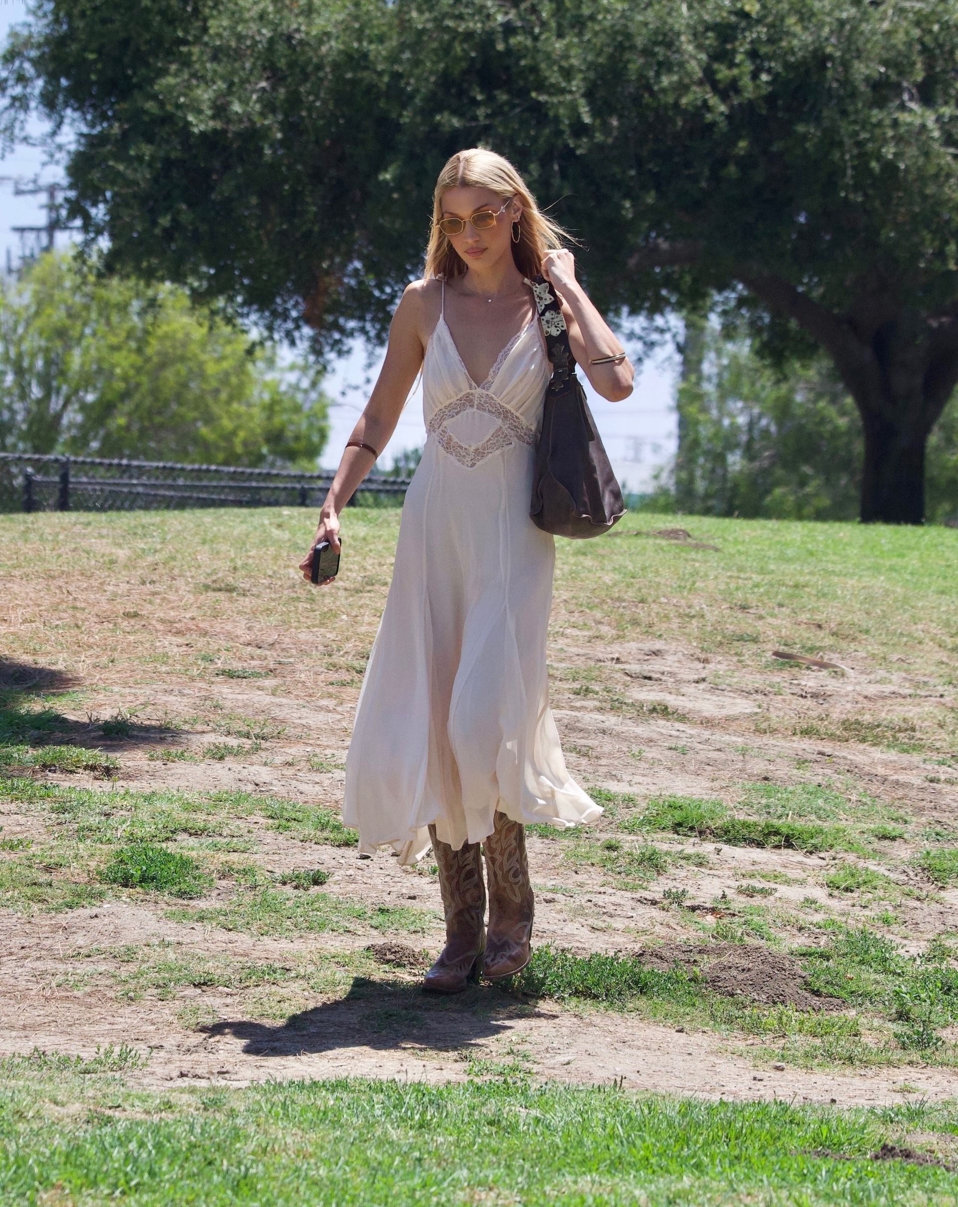 Bella Hadid was spotted at a park in Los Angeles. She wore cowboy boots with a summery white nightgown dress and a brown bag.