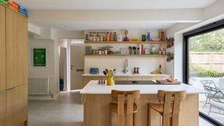 open plan kitchen with open shelving, light oak cabinets, and a hob on the island