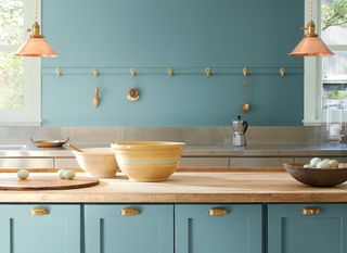 A kitchen with wooden and steel worktops complete with brass detailing is contrasted against a light blue Aegean Teal Benjamin Moore paint painted on the walls