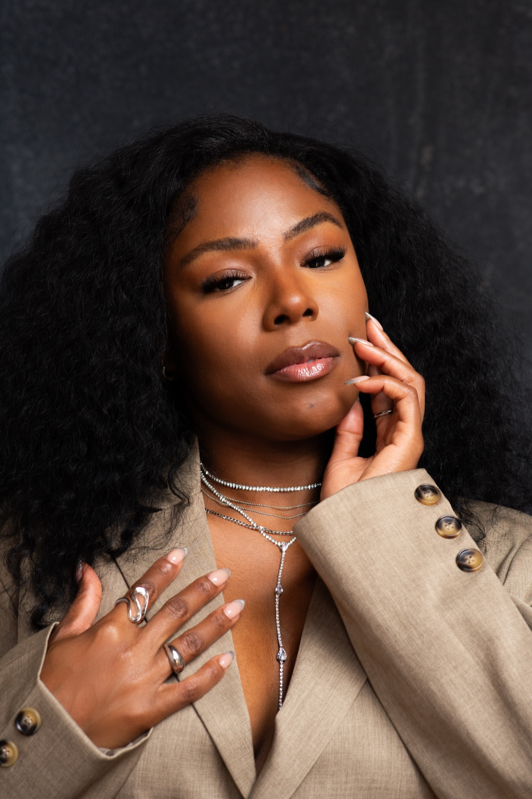 a black woman in a tan jacket with black curls and a diamond necklace