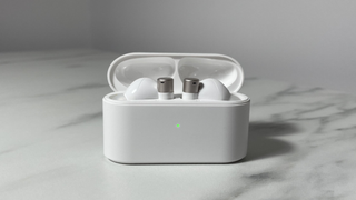 White and silver 1More PistonBuds Pro Q30 earbuds sitting in the charging case with the lid open. The case is sitting on a white marble-effect desk.