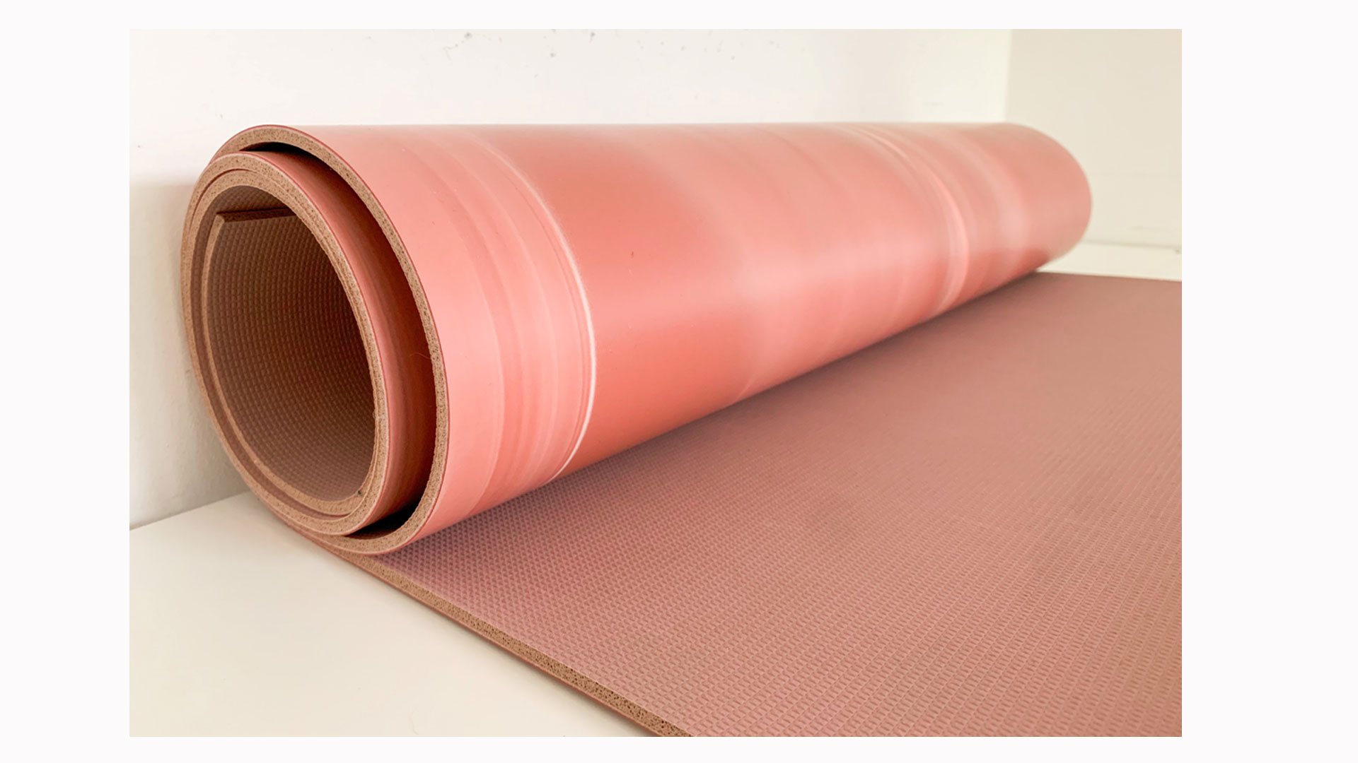 La imagen muestra una esterilla de yoga Lululemon reversible rosa de 5 mm medio desenrollada.