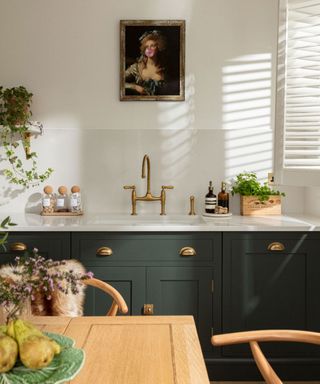 Green painted kitchen cabinets with gold hardware and gold tap and quirky artwork hung on white wall