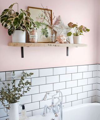 Pink bathroom with white metro tiled wall and wooden shelf with plants on it
