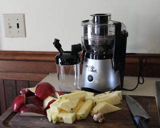 Magic Bullet mini juicer with chopped pieces of red apples and pineapple pieces on wooden chopping board