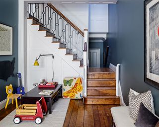 A dark blue-gray kids' room idea with playroom area, white staircase and dark wood floors.
