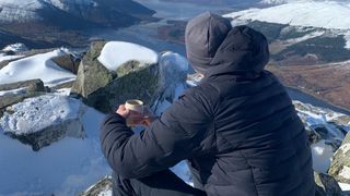 A hiker drinks coffee on a snowy summit