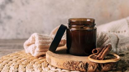 A candle in an amber glass jar on a wood round beside a folded sweater 