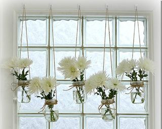 Five mason jars filled with floral arrangments and suspended from a height with string on coat hooks as window display