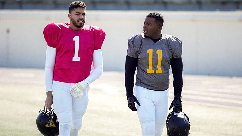 Michael Evans Behling as Jordan Baker and Daniel Ezra as Spencer James in uniform on the football field in All American season 5