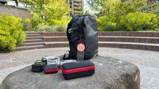 Shot of the Stratus Photo Backpack resting on a rock. A variety of carry cases and gadgets sit around it.