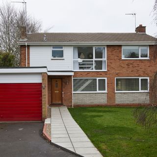 four bedroom 1970s house exterior with red garage door and driveway