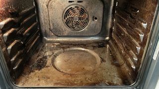 Dirty oven with door open and racks and trays removed to show a key step for how to clean an oven with baking soda