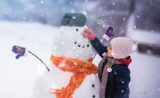 A young child sticking a carrot onto a snowman's face for the nose.