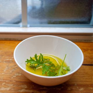 White bowl on a windowsill full of citronella leaves and oil