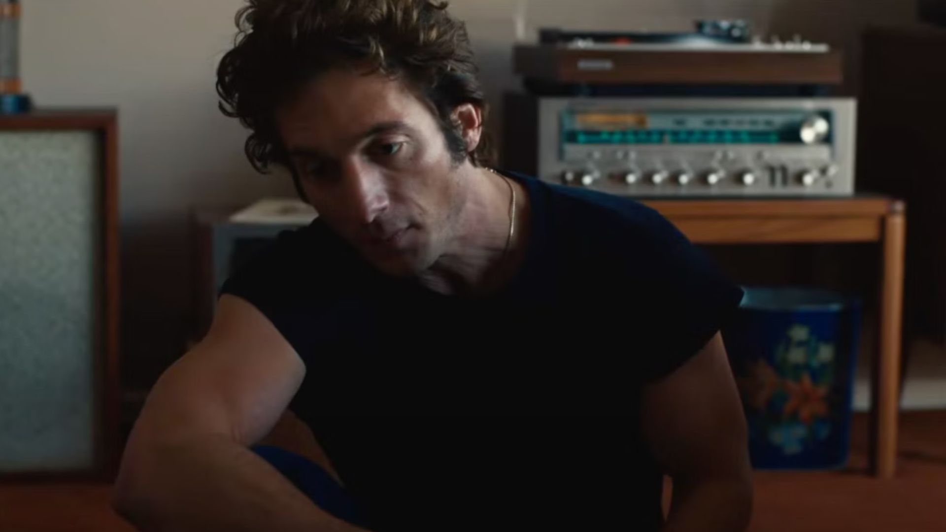 an image of jeremy allen white playing bruce springsteen in the movie Deliver me from Nowhere. He is sitting on a low seat at home listening to music
