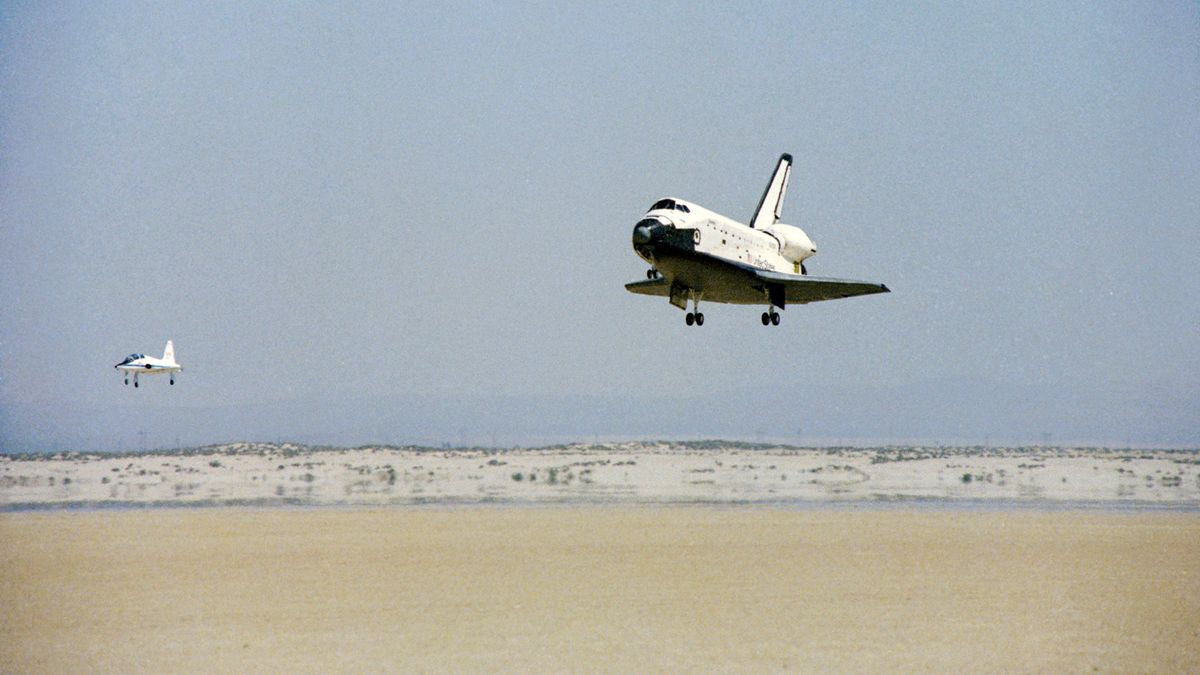 space shuttle landing in the desert with a chase plane in front