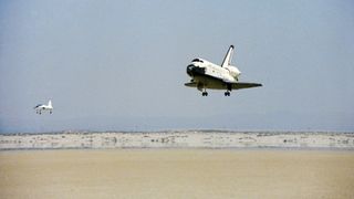 space shuttle landing in the desert with a chase plane in front