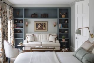 An example of how to make a small bedroom look bigger in a blue scheme with built-in shelving and a small white sofa.