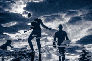 Reflections of people in water on a beach.