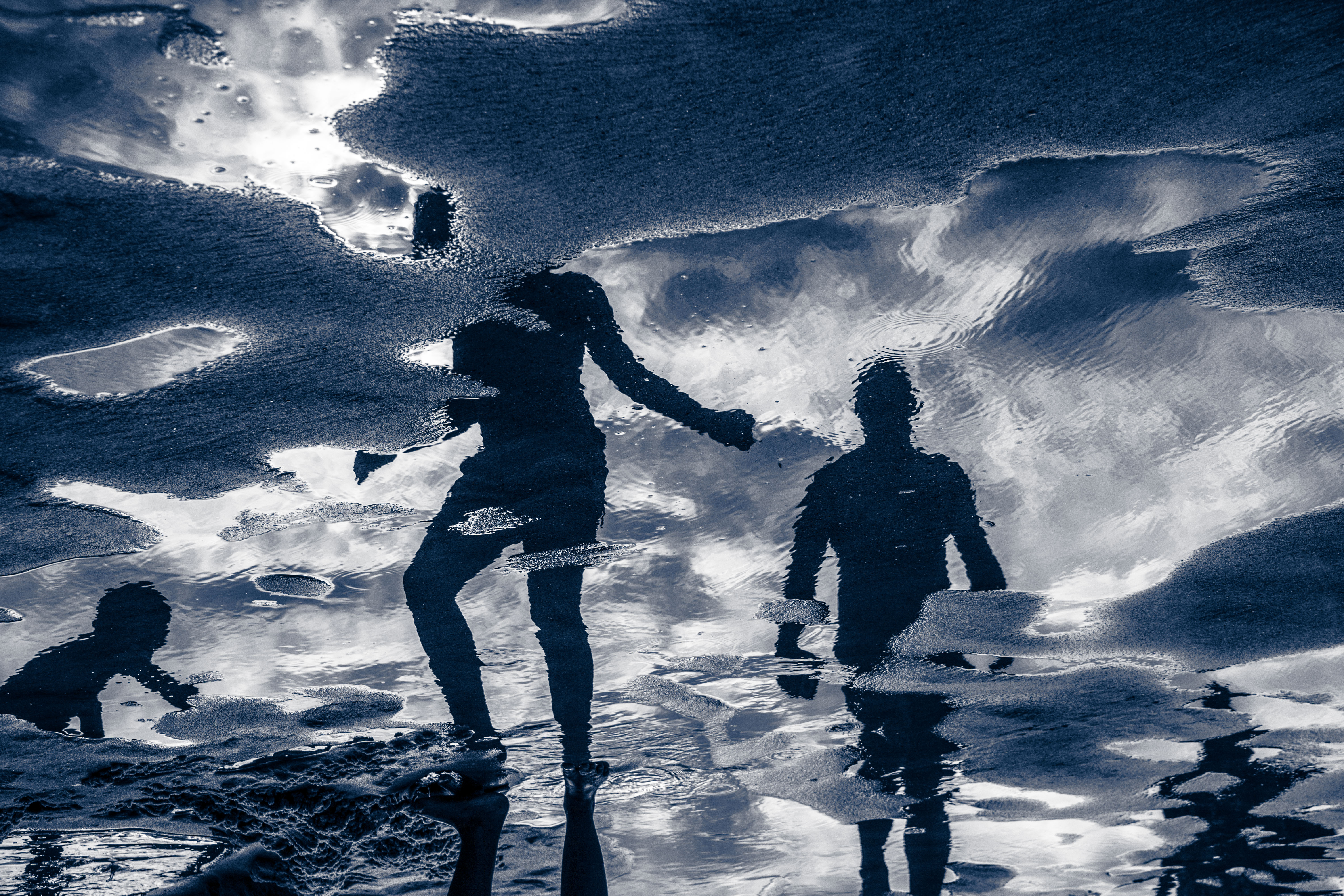 Reflections of people in water on a beach.