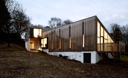 Wooden home with large windows on a hill near the woods 