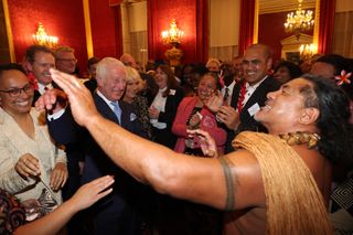 King Charles dancing with a Samoan rugby player surrounded by Queen Camilla and clapping guests