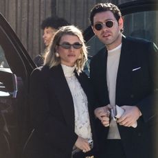 Sofia Richie wears a Schiaparelli two piece skirt set with a black coat, black bag and gold shoes.